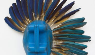 an abstract mask-like sculpture made of a blue plastic jug and blue and tan feathers