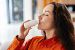 A woman drinks from a small bottle of yogurt.
