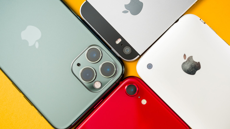 A collection of vintage iPhones. From the left: a midnight green iPhone 11 Pro, space gray iPhone 5s, white iPhone 3G and a red iPhone SE.