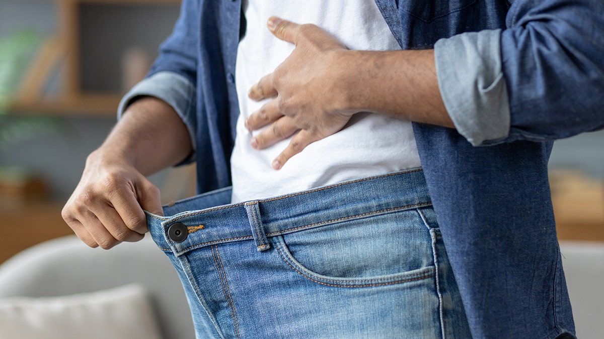 man holds out jeans with thumb