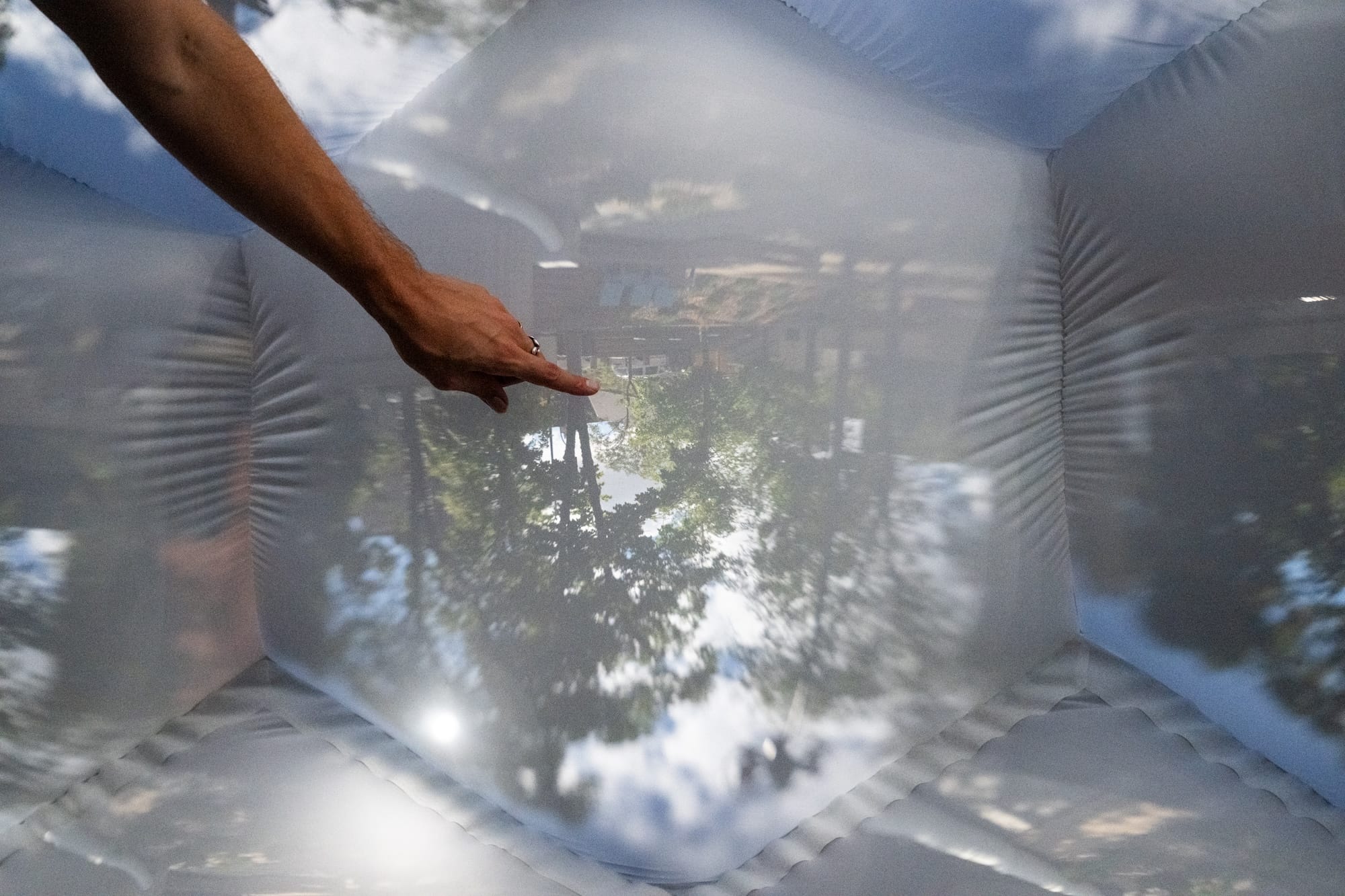 the interior of an architectural, inflatable compound camera installation with a hand pointing at a bubble-like form featuring an image of outside captured by a tiny aperture