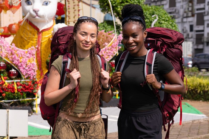 race-across-the-worl Ella Eyre and Nana stood next to each other with large red backpacks, smiling ahead.