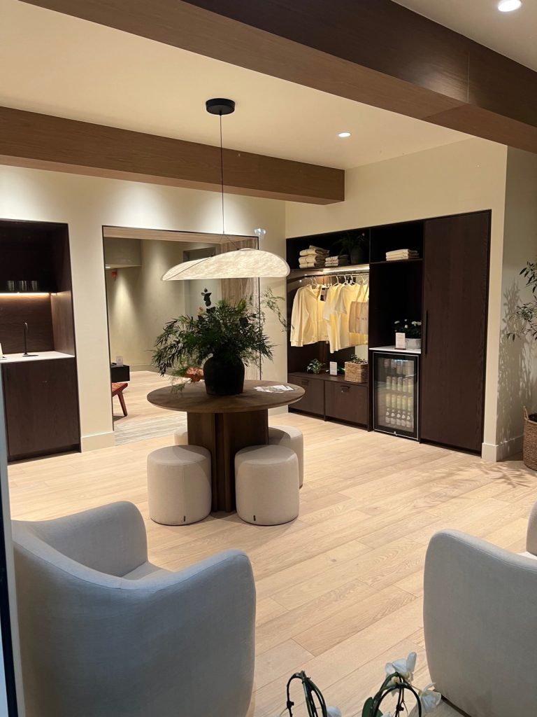 Front area of Sculpt House with two armchairs, a round table and stools, a rail of Pilates clothes and a drinks fridge