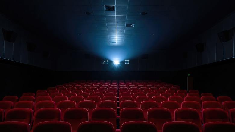 Empty cinema with row upon row of empty red seats, with the bright glare of the projector in the back.