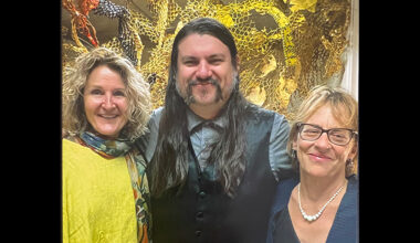 Two faculty members stand with their former student at his art exhibition.