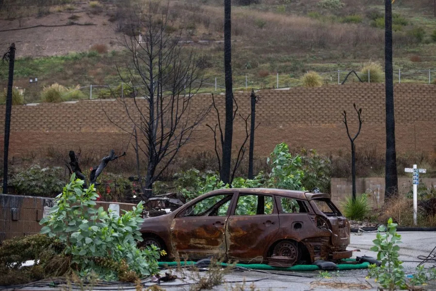 Rain comes down on a burnt vehicle in the Palisades Fire zone on Saturday, Nov. 15, 2025, in the Pacific Palisades section of Los Angeles. (AP Photo/Ethan Swope)