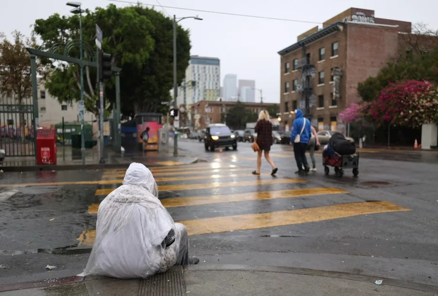 Los Angeles, CA – November 14: An unhoused individual sits on the curb during a storm in the Skid Row area of downtown Los Angeles on Friday, Nov. 14, 2025. (Eric Thayer / Los Angeles Times via Getty Images)