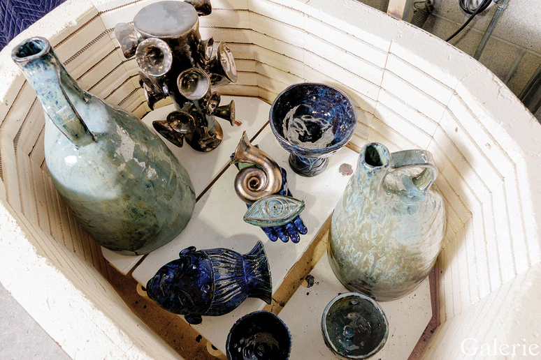 Pottery pieces with blue and green glazes displayed in a kiln, including vases, bowls, and decorative items.