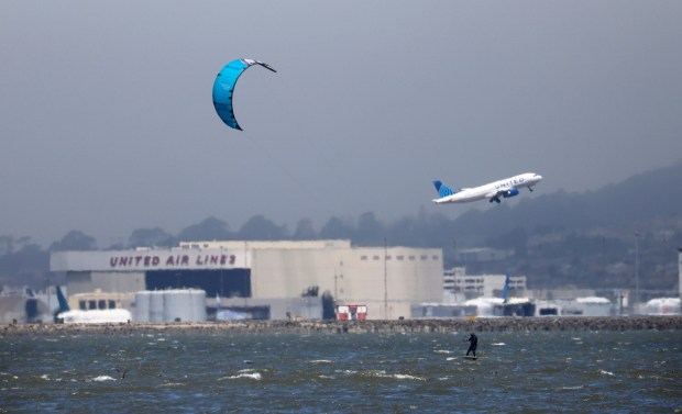 A kite surfer surfs on the water near San Francisco International Airport as seen from Coyote Point Recreation Area in San Mateo, Calif., on Sunday, July 20, 2025. The Bay Area is expected to continue experiencing cool and cloudy weather. The highest temperature expected in the region this week is 82 degrees in Brentwood, forecasted for mid-week. (Nhat V. Meyer/Bay Area News Group)