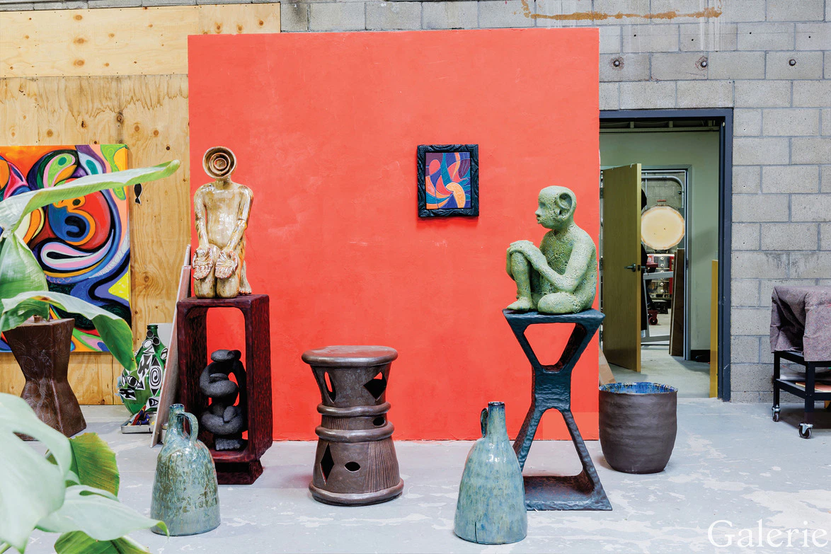 Art display with various sculptures and a painting against a bright red wall in an indoor gallery setting.