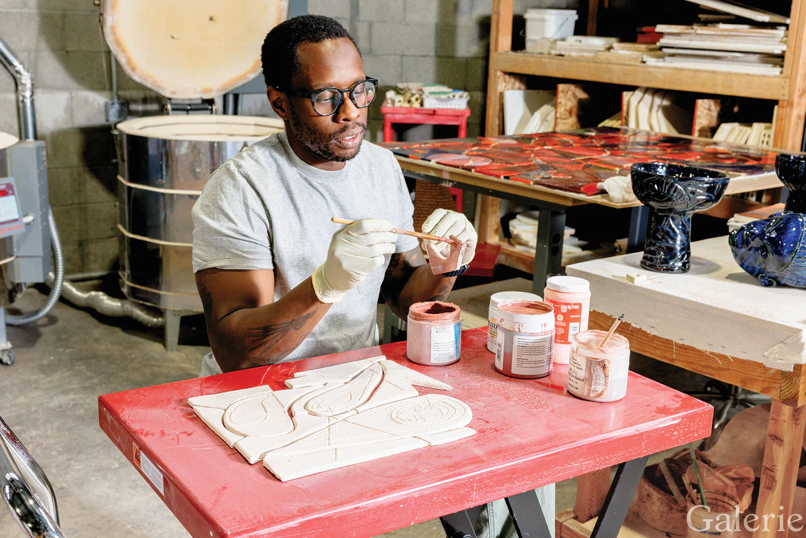 Person sitting at a table painting a ceramic piece with brushes in a workshop setting.