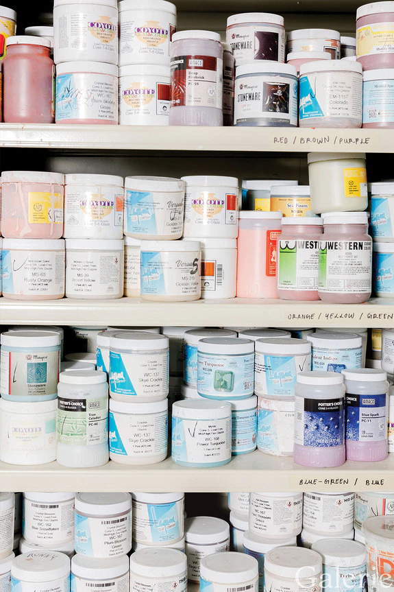 Shelves stacked with various colorful containers of paint supplies in a store or studio setting.