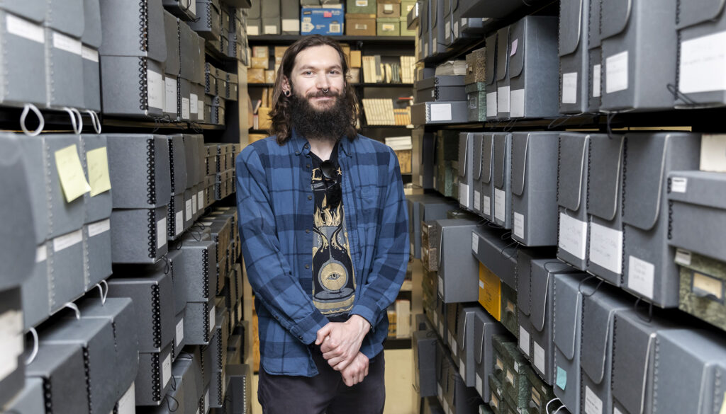 Tyler Lee-Wynant stands among shelves lined with boxes of archival materials in the California Language Archive