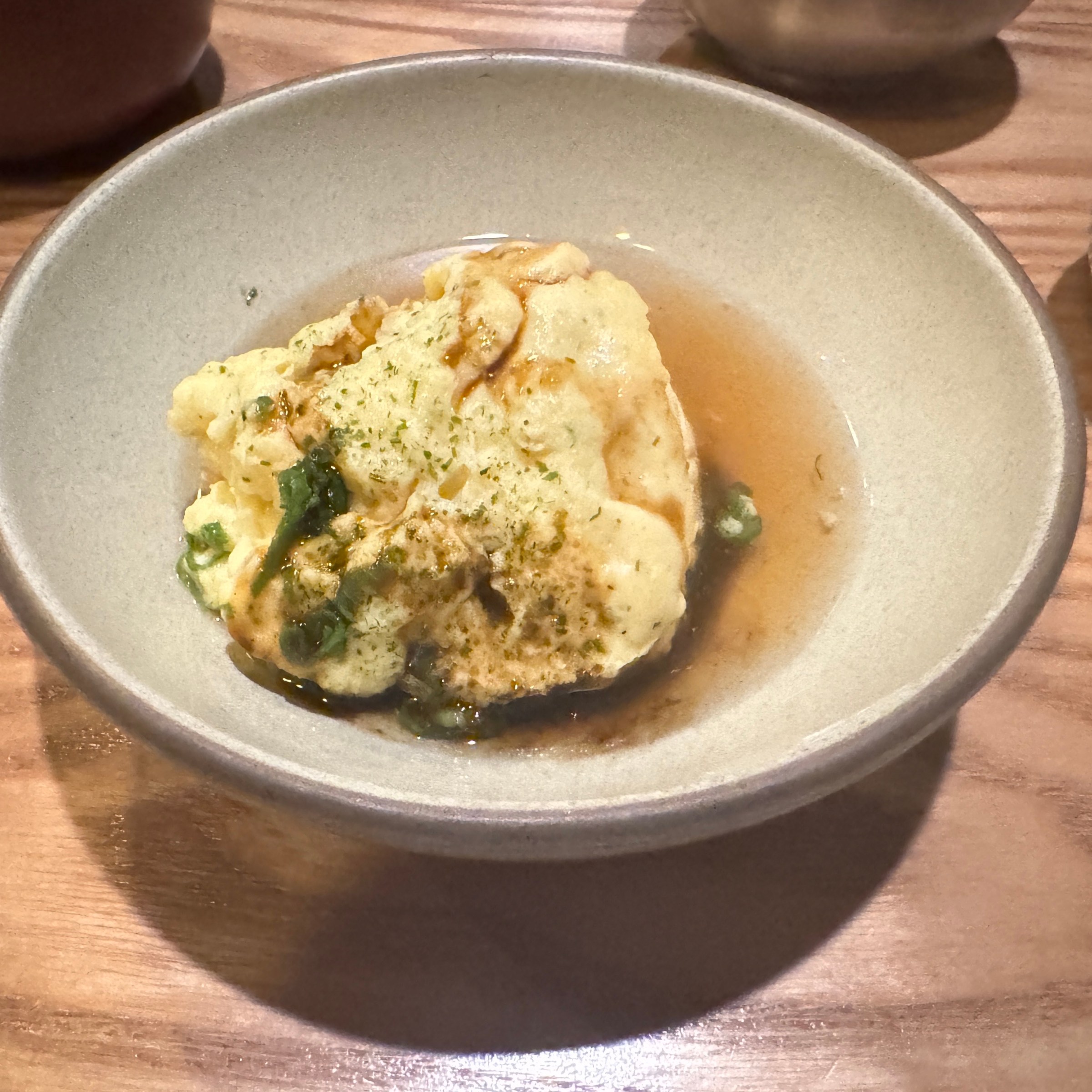 A piece of savory egg souffle in a bowl with broth at San Ho Won in San Francisco.