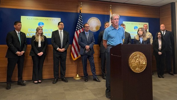Chris Heise stands next to San Diego County District Attorney Summer Stephan while talking about his experience being scammed out of $35,000 Tuesday. (Alex Riggins/The San Diego Union-Tribune)