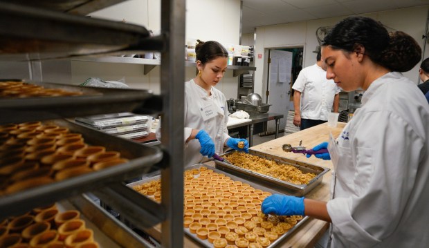 Elliana Nylund, left, and Lily Flores, right, make mini apple tarts in the Prado restaurant kitchen in Balboa Park on Wednesday, Nov. 19, 2025, to be served at their school's Thanksgiving luncheon and fundraiser Thursday. The money raised will help support their school's culinary arts and other programs. (Howard Lipin / For The San Diego Union-Tribune)