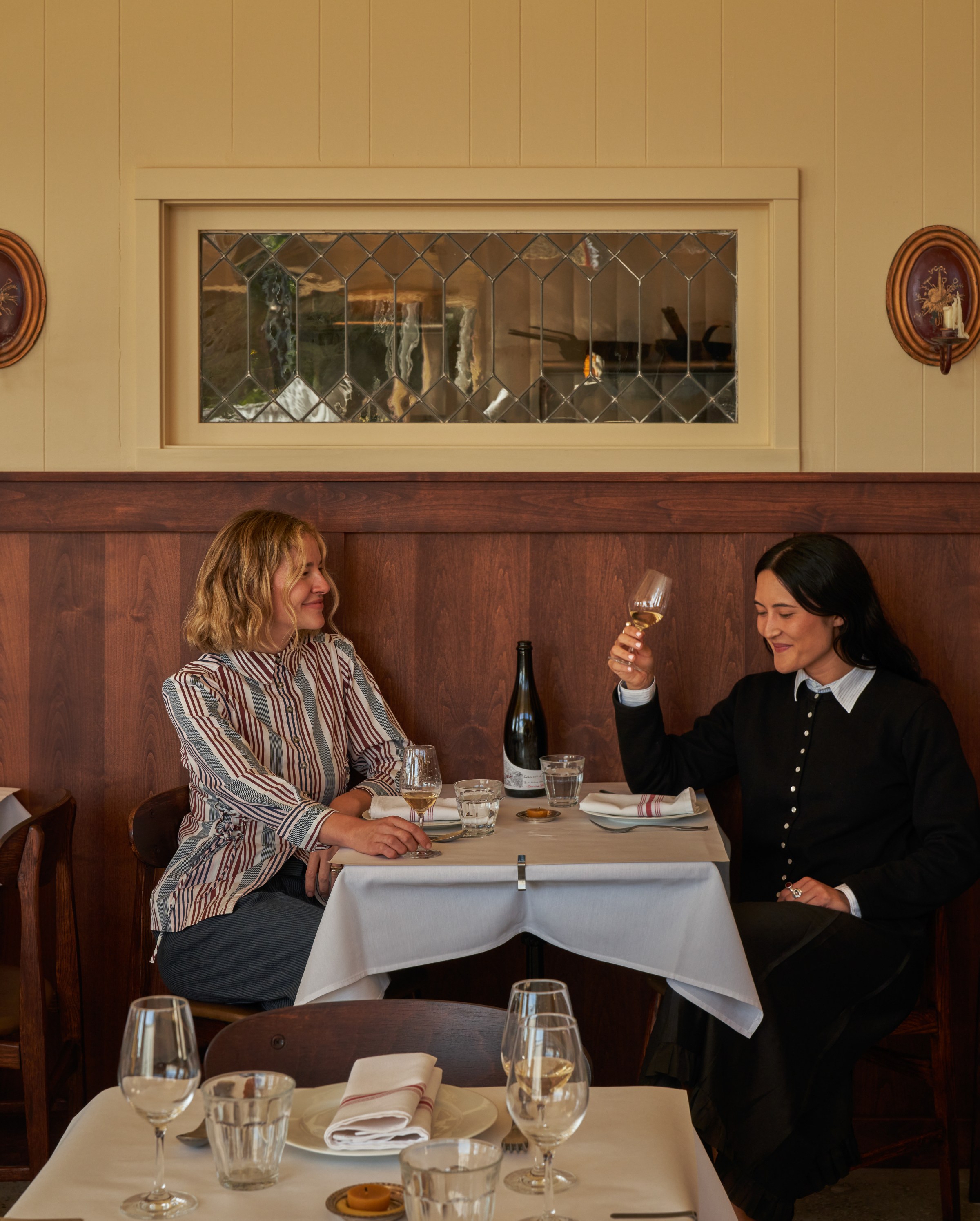 Two women sitting at a table at Wilde’s holding glasses of wine