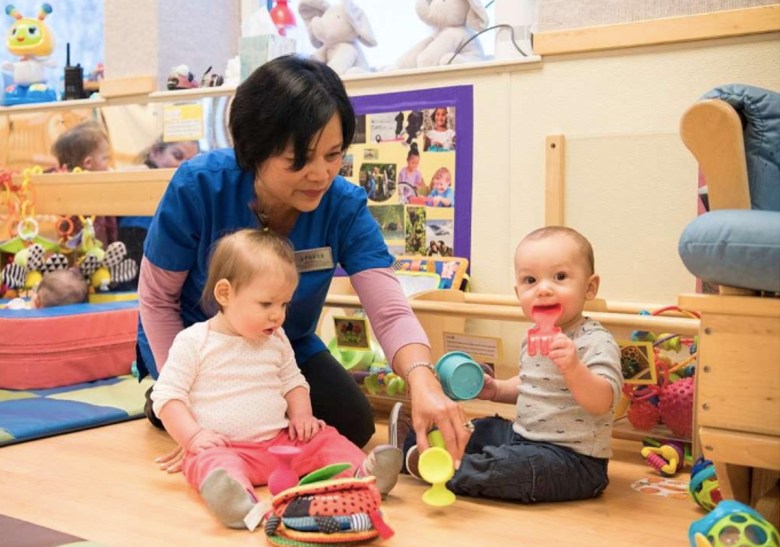 A woman sits in a floor in a playroom with toys and two babies.