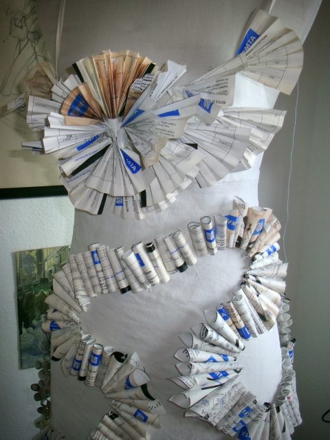 A dress form decorated with folded and rolled pieces of paper, including repurposed parking tickets, creates a striking pattern across the bodice and waist.