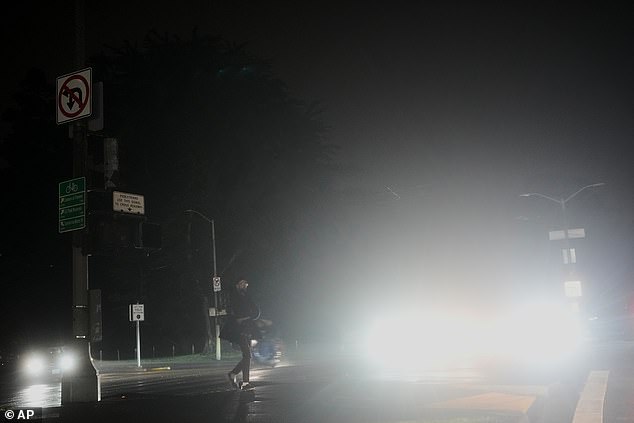 A pedestrian crosses an intersection lit with headlights amid the San Francisco power outage