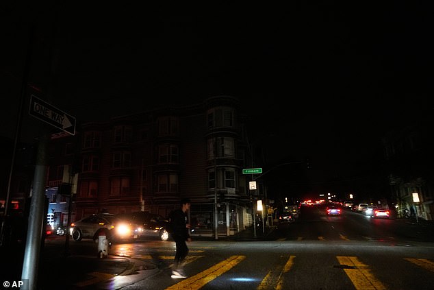 A pedestrian uses a flash light while crossing an intersection as outages darken the streets