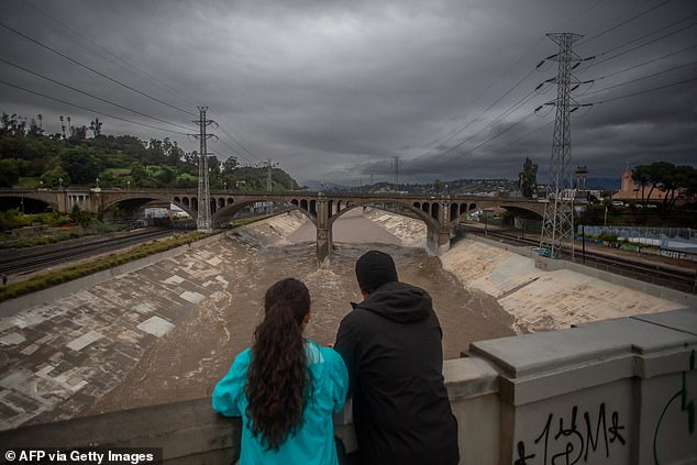 By Wednesday night, flash flood warnings - which are issued when floods are imminent or already happening - were in effect for several cities in Los Angeles County. A couple is pictured watching the high water level of the Los Angeles river on Wednesday