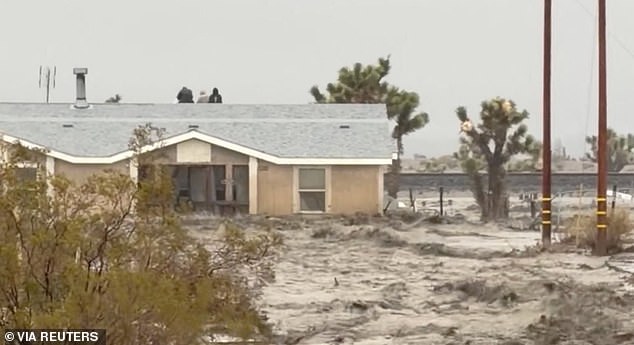 People sit on the roof of a building while they are stranded during floods partially submerging the surrounding area in the aftermath of torrential rains, in San Bernardino County