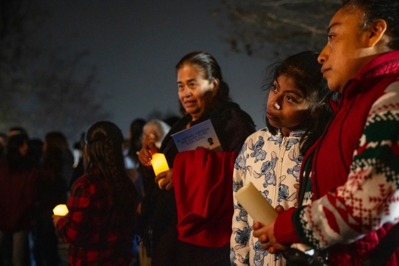 People gathered at night, holding candles and looking thoughtful.