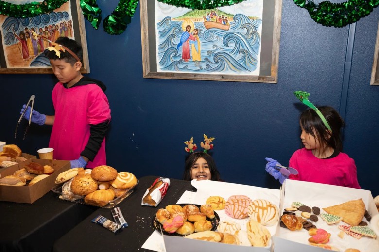 Three children with festive headbands behind a table of assorted pastries and breads.
