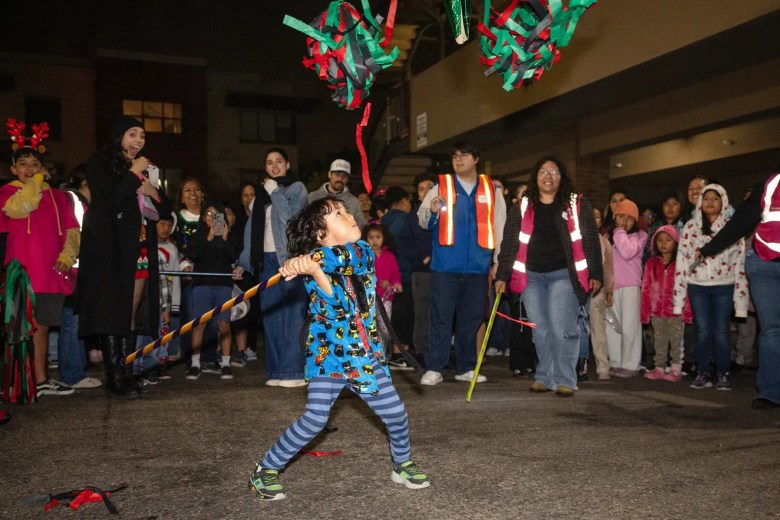 A child swings a stick at a piñata while a crowd watches at night.