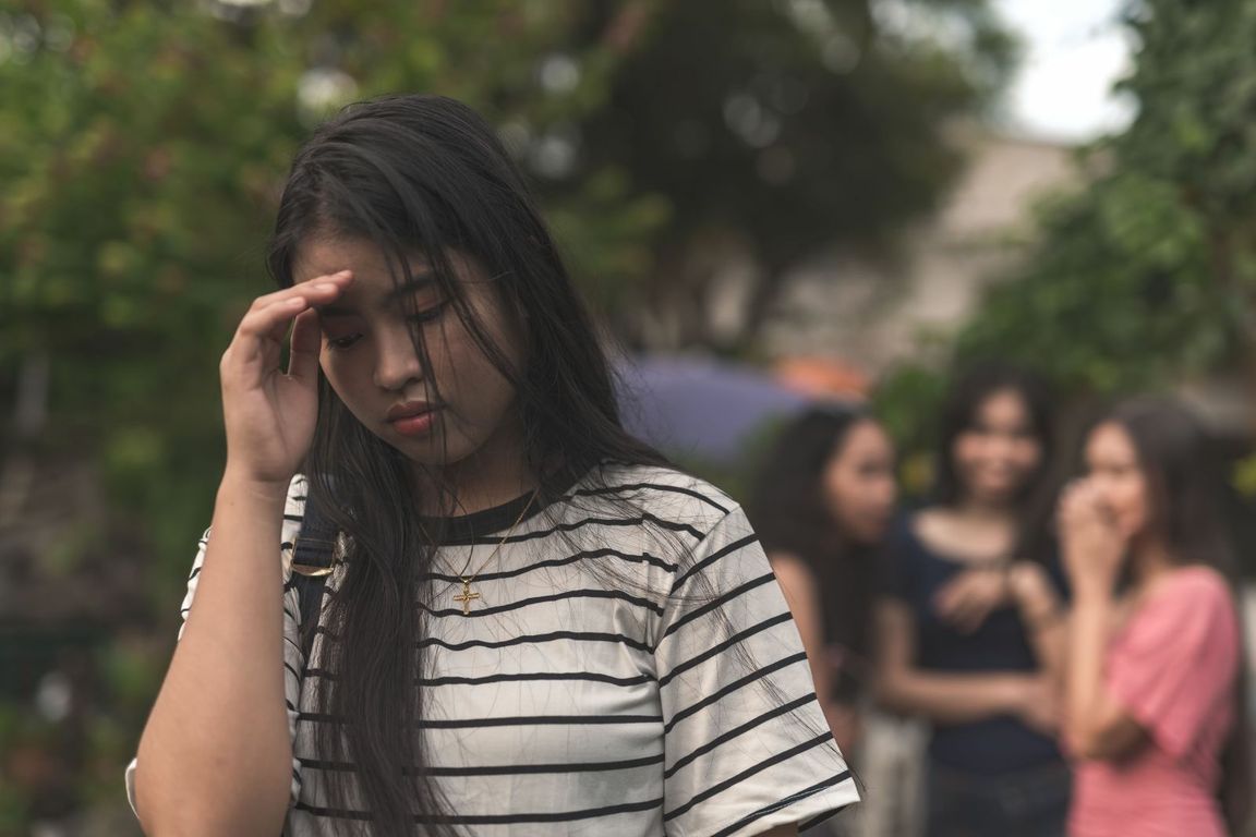 Asian woman upset in the foreground with a group of women excluding her in the background