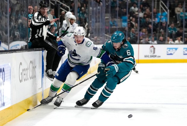SAN JOSE, CALIFORNIA - NOVEMBER 28: Drew O'Connor #18 of the Vancouver Canucks and Sam Dickinson #6 of the San Jose Sharks battle for control of the puck in the first period at SAP Center on November 28, 2025 in San Jose, California. (Photo by Thearon W. Henderson/Getty Images)