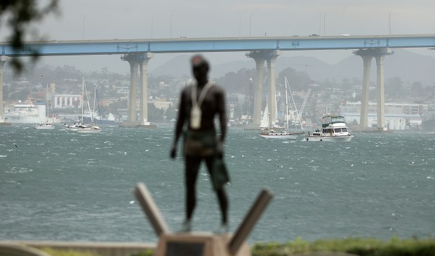Coronado, CA_12_24_25_|Whitecaps formed in windy weather and stressed sailboats at anchor in this view looking toward the San Diego-Coronado Bay Bridge with the Naked Warrior US Navy SEALs statue in the foreground. |Heavy weather from a Pineapple Express storm hit Coronado before noon downing branches and causing major whitecaps to form in San Diego Bay and two sailboats to drag anchor in Glorietta Bay. (John Gastaldo / For The San Diego Union-Tribune)