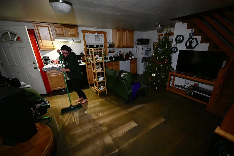 A resident sweeps water and mud in her house after flooding Wednesday, Dec. 24, 2025, in Wrightwood, Calif