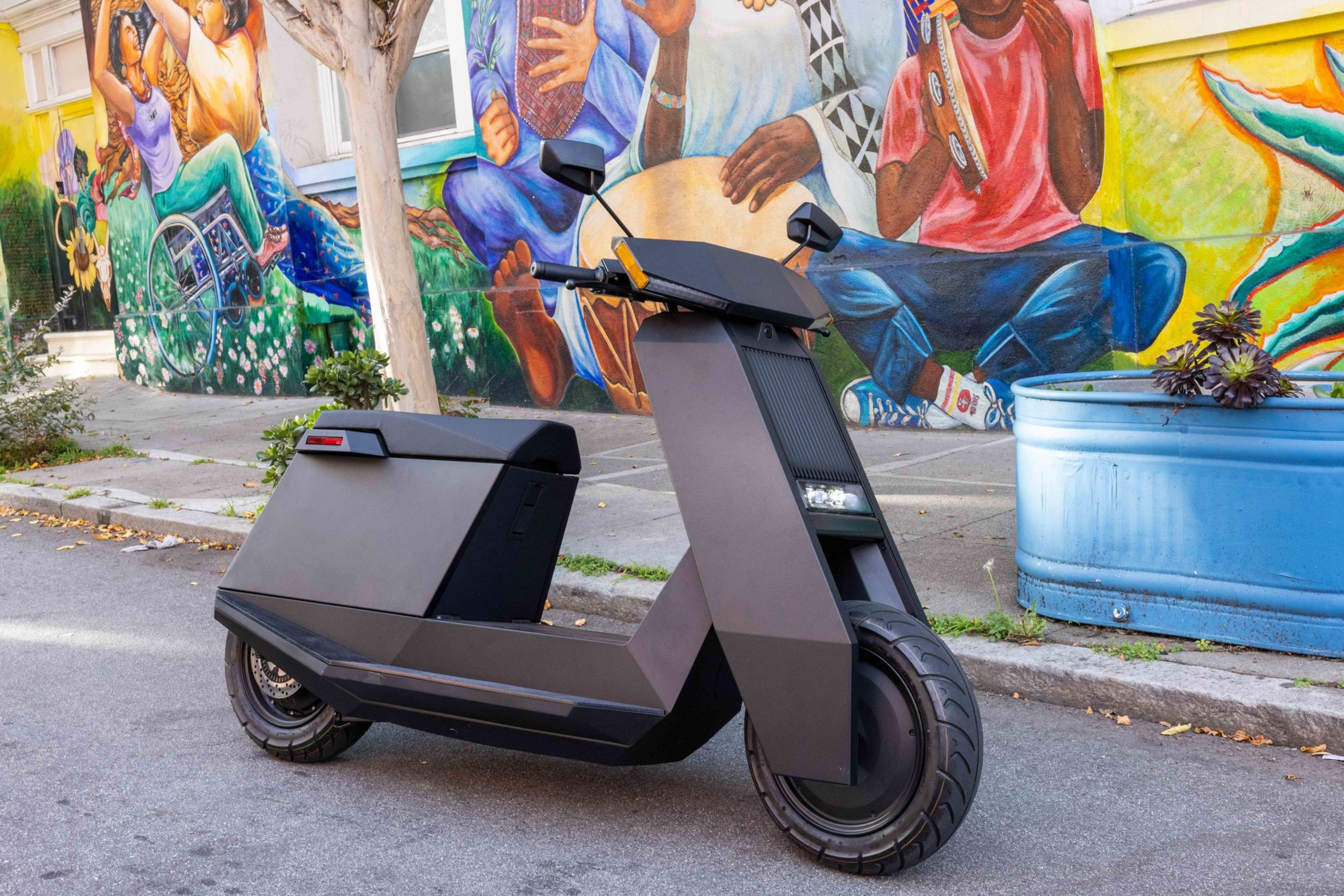A sleek black electric scooter is parked on a street beside a colorful mural of people playing music and dancing.