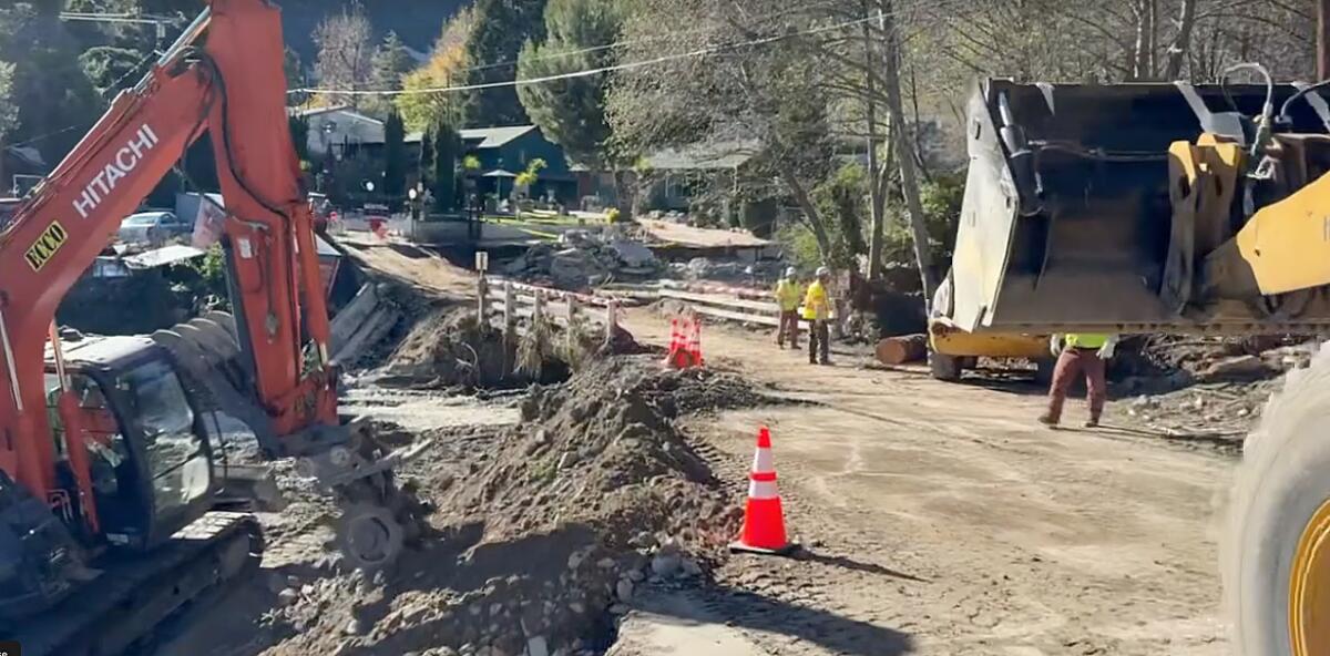 Bulldozers and people in yellow vests stand next to a dirt bridge.