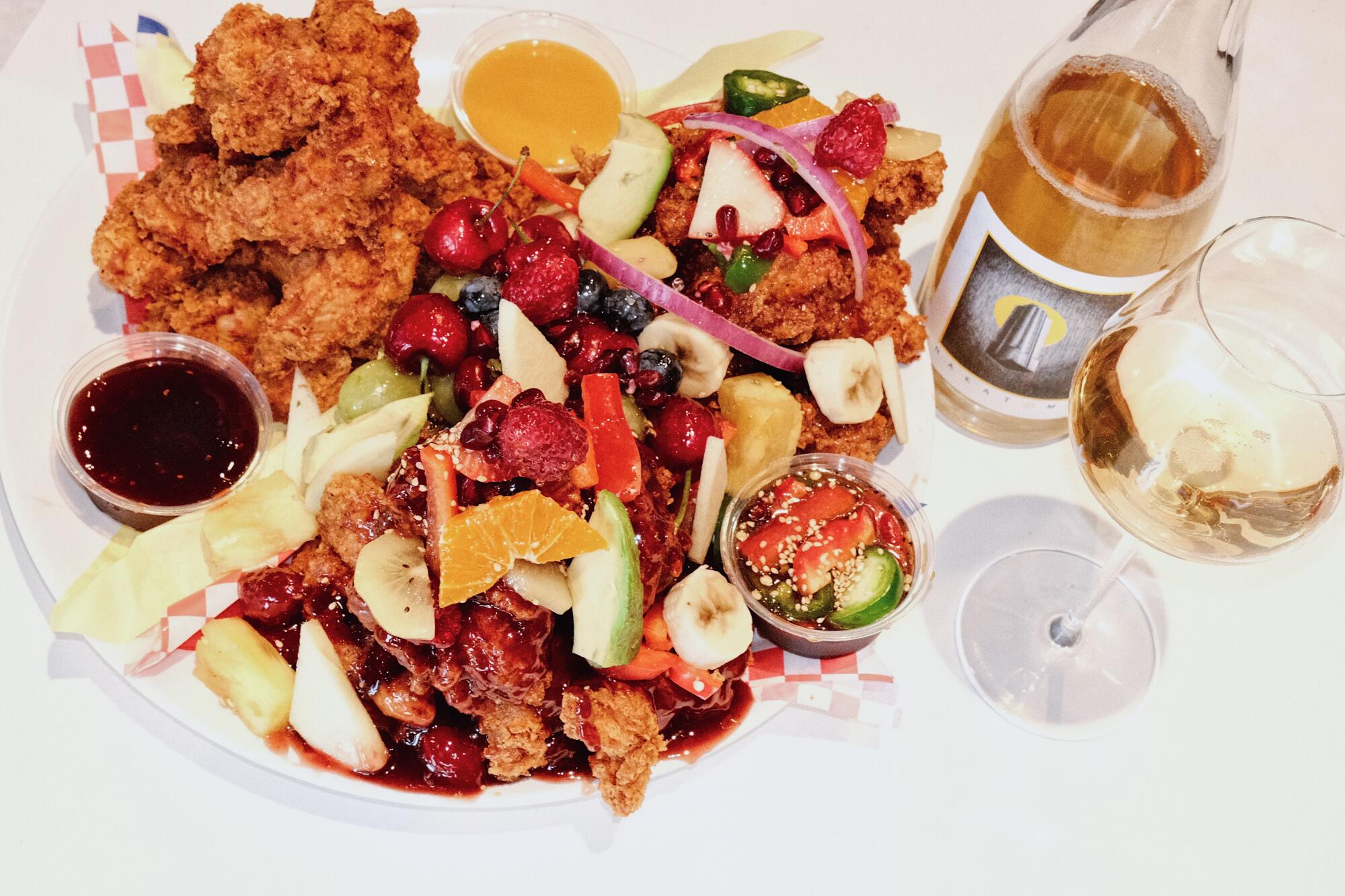A platter of Gol Tong fried chicken, smothered in fruit and sauces, paired with a bottle and glass of white wine on a table