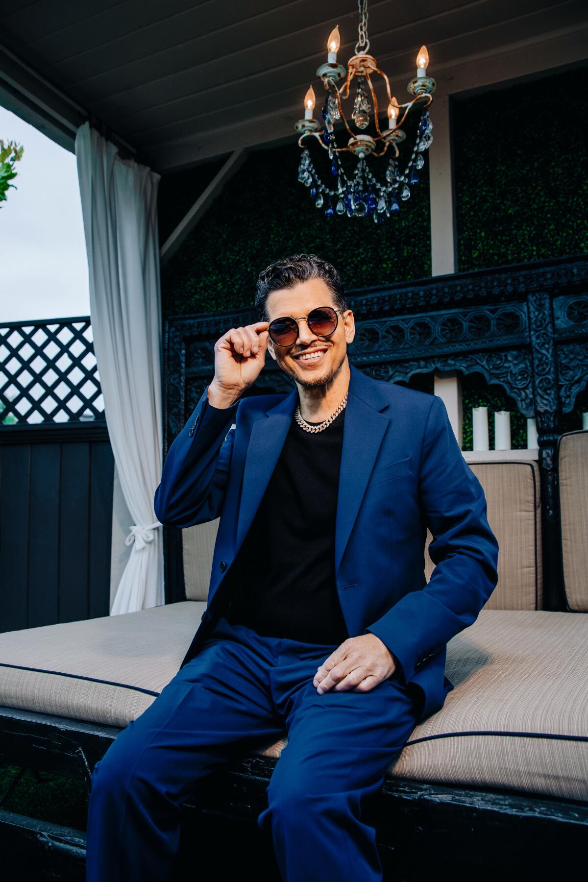 Man in blue suit and sun glasses sitting on a couch outside