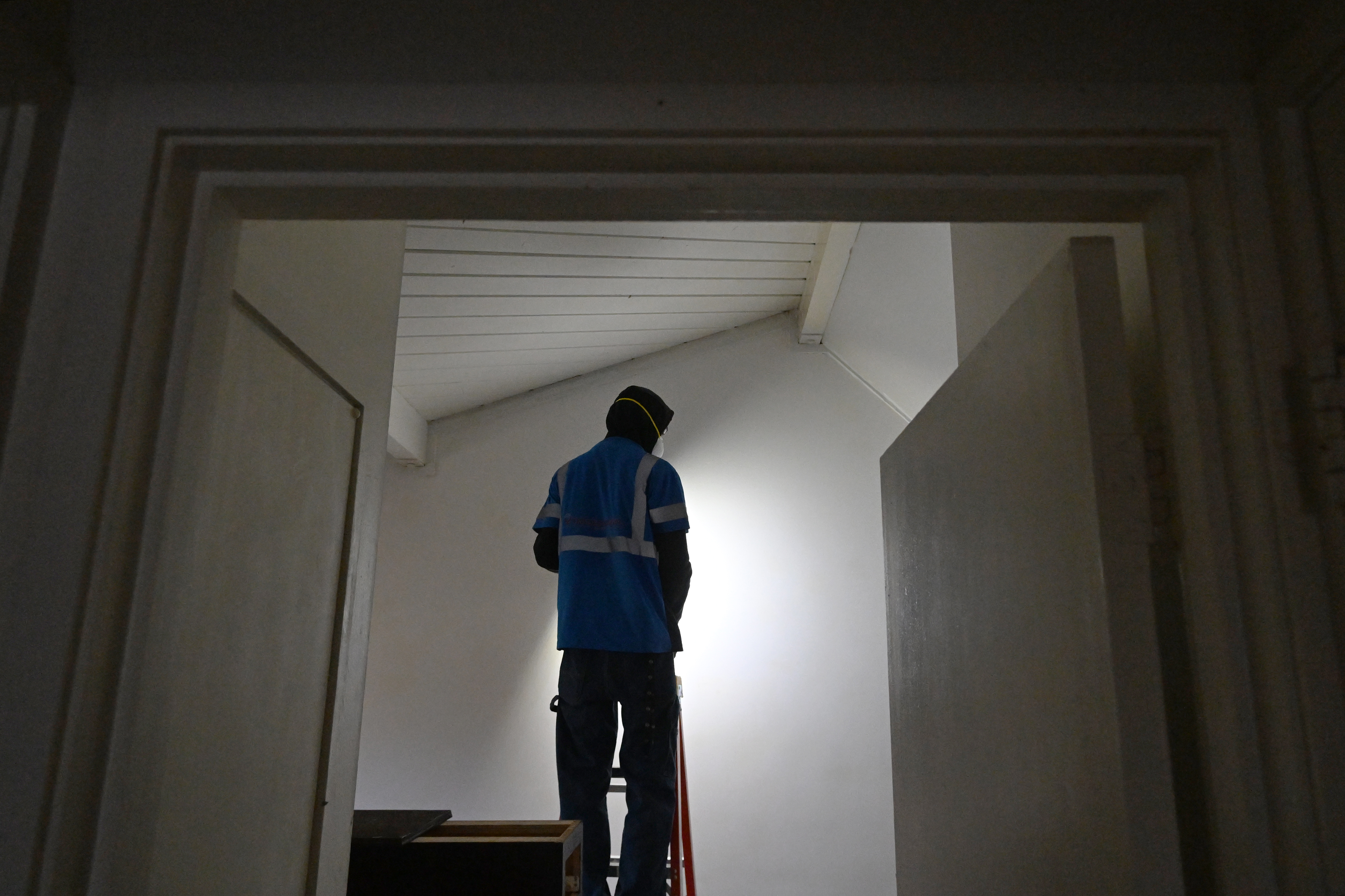 A construction trainee sands a wall inside one of the...