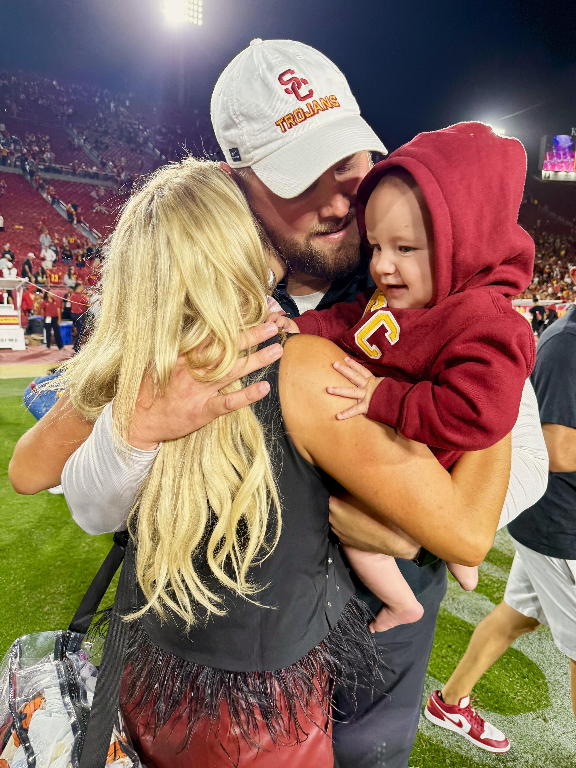 USC assistant coach Zach Hanson embraces his wife, Annie, and son, Rock, share a hug on the field at the Coliseum.