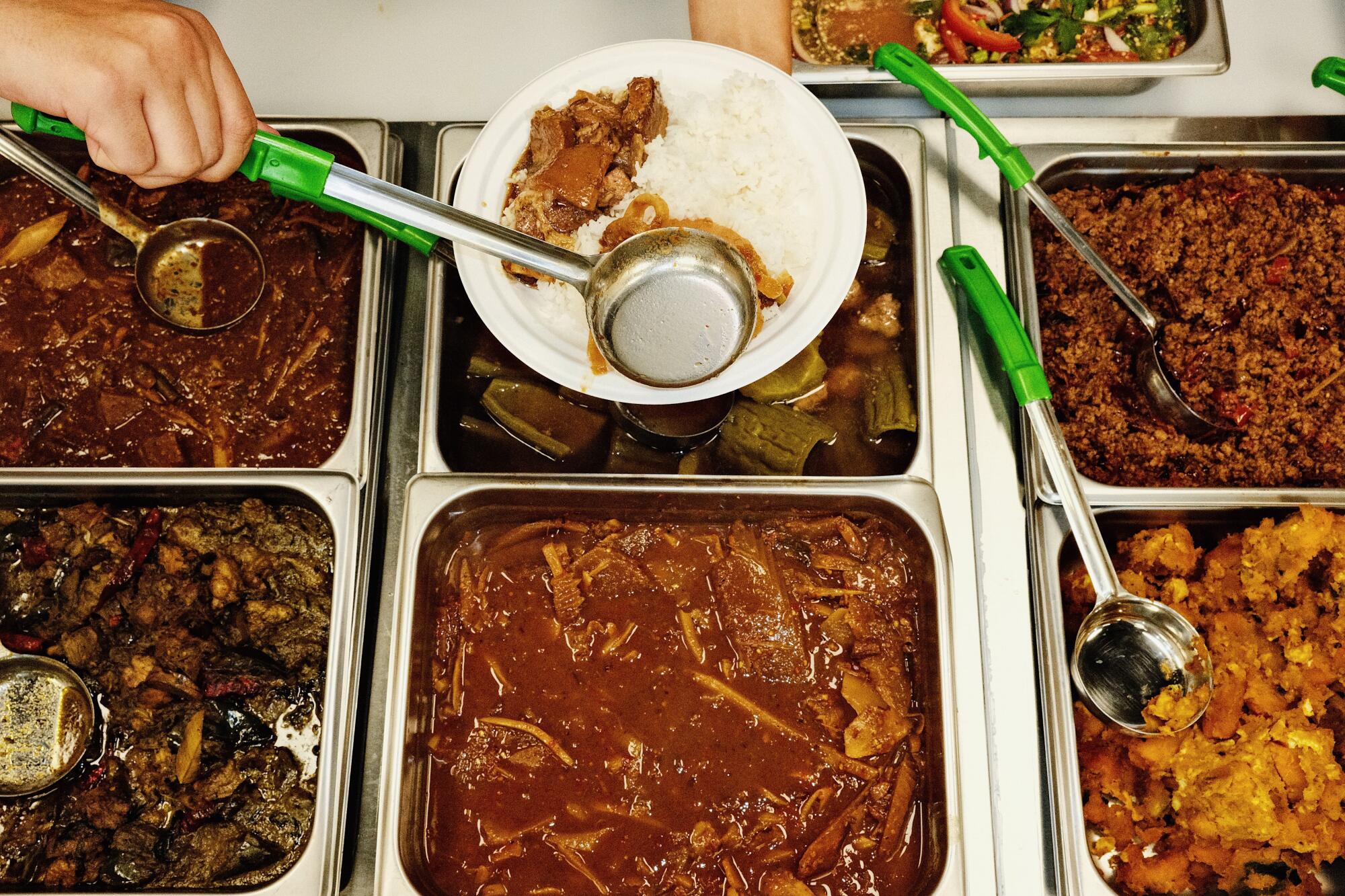 A hand spoons curry onto a plate at the steam table at Luv2Eat Express in Hollywood.