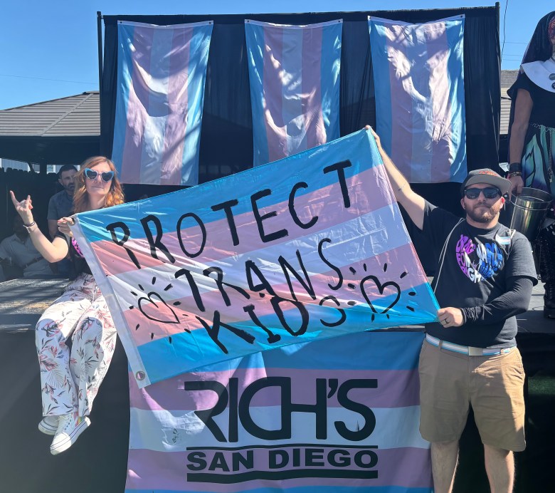 Two people hold a transgender flag with a message reading PROTECT TRANS KIDS in San Diego