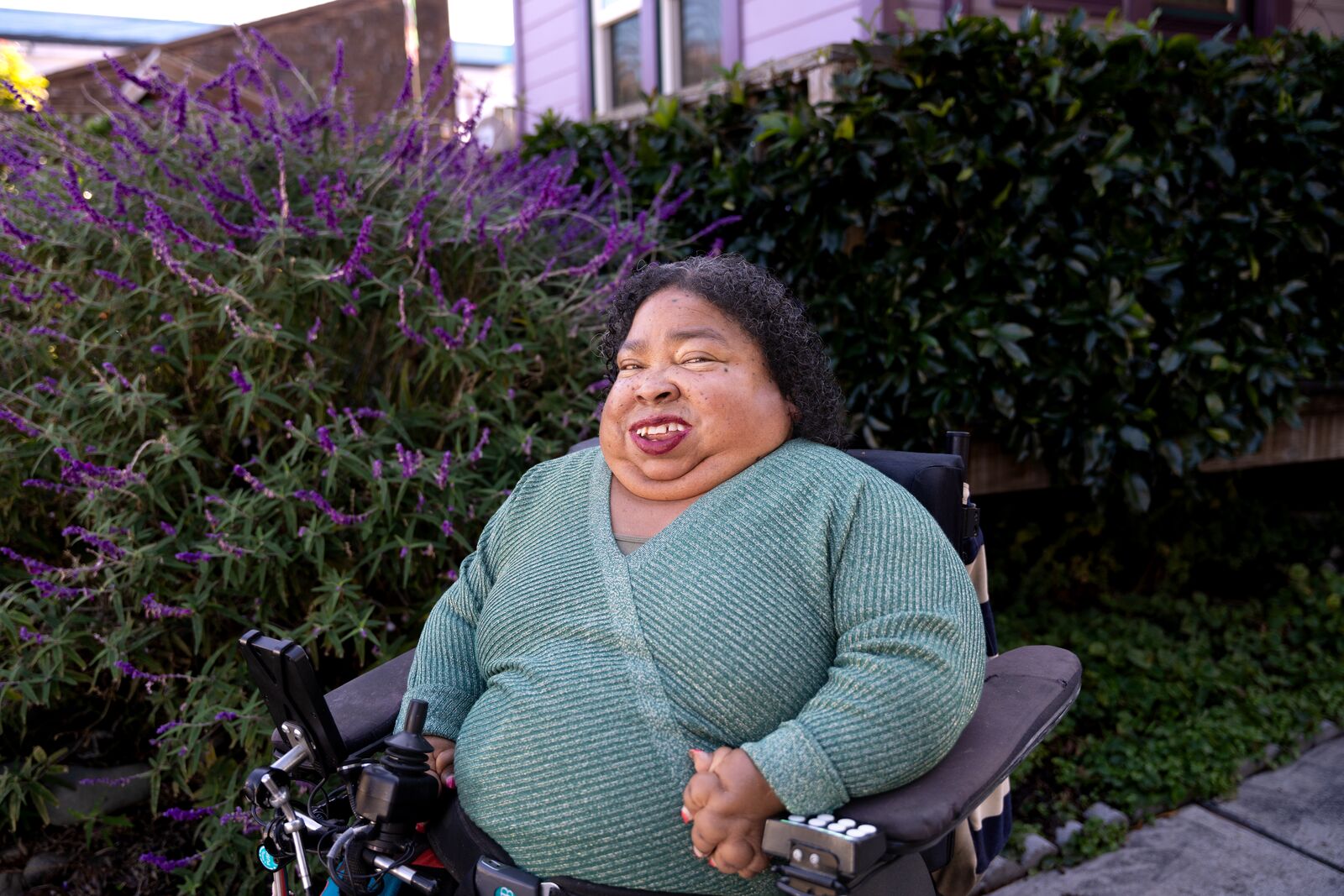 A woman in a wheelchair smiles in front of lavender flowers.