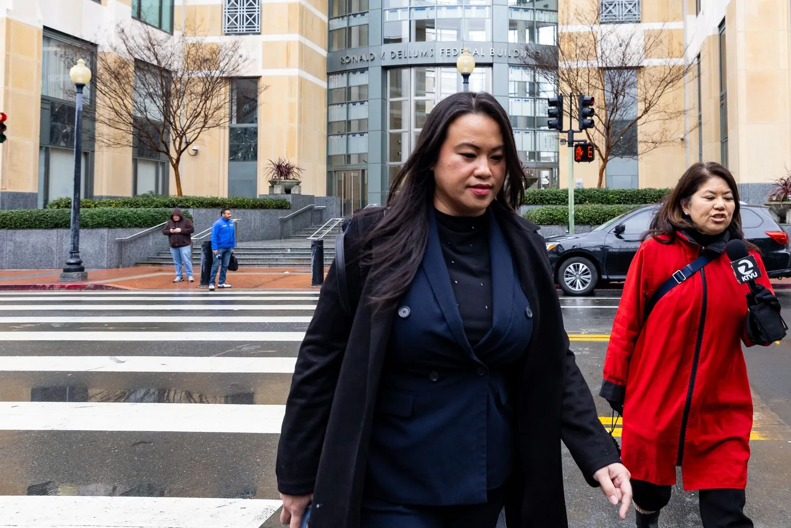 Sheng Thao walks across a street followed by a TV news reporter.