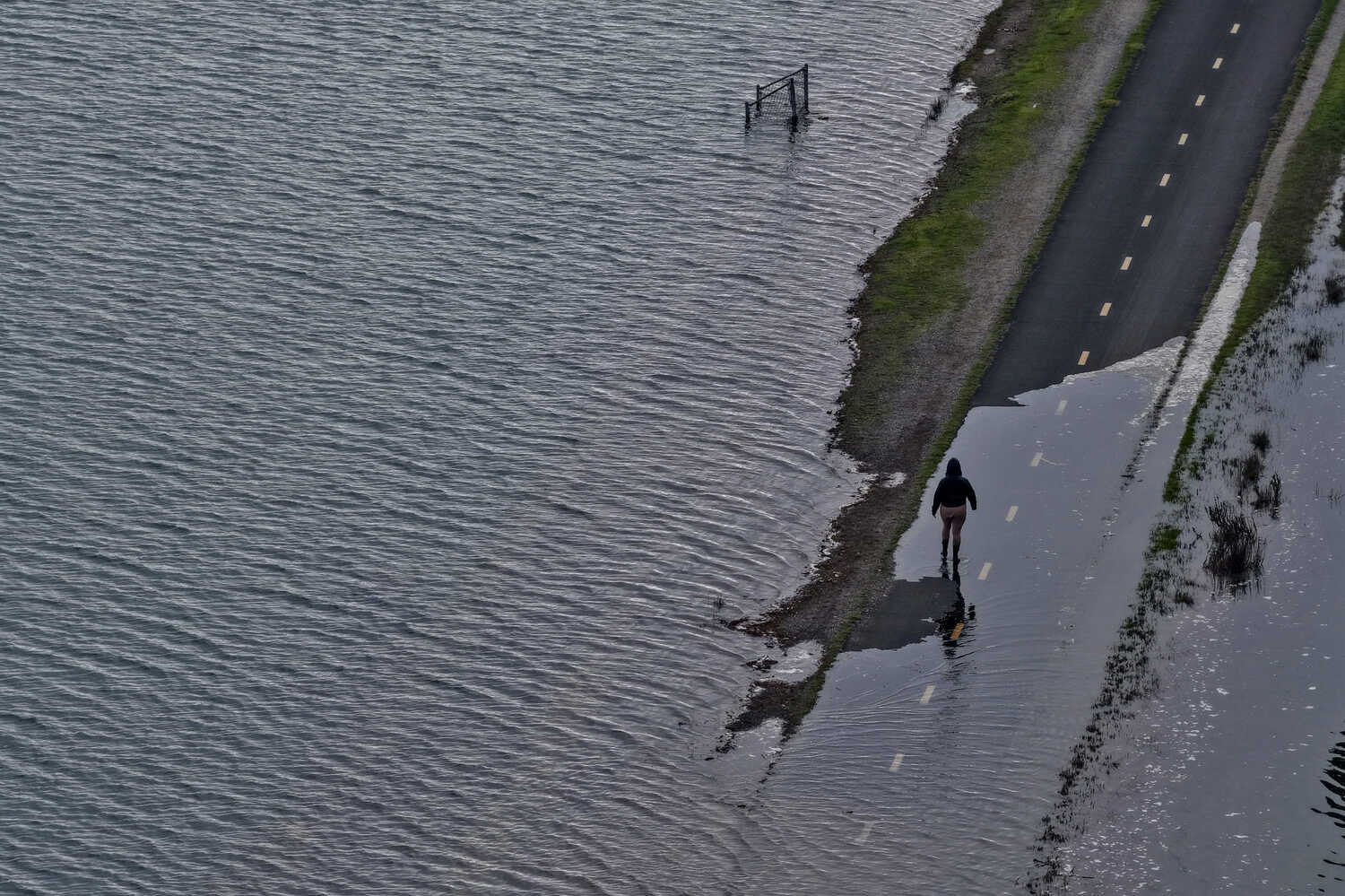 A person walking along a flooded road near a body of water.