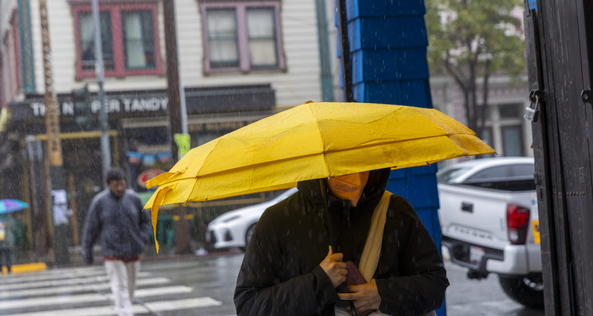 A person walks down the street towards the camera. Their umbrella covers their face.