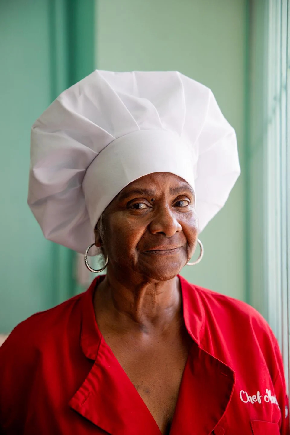 A woman in a chefs hat looks to the camera.
