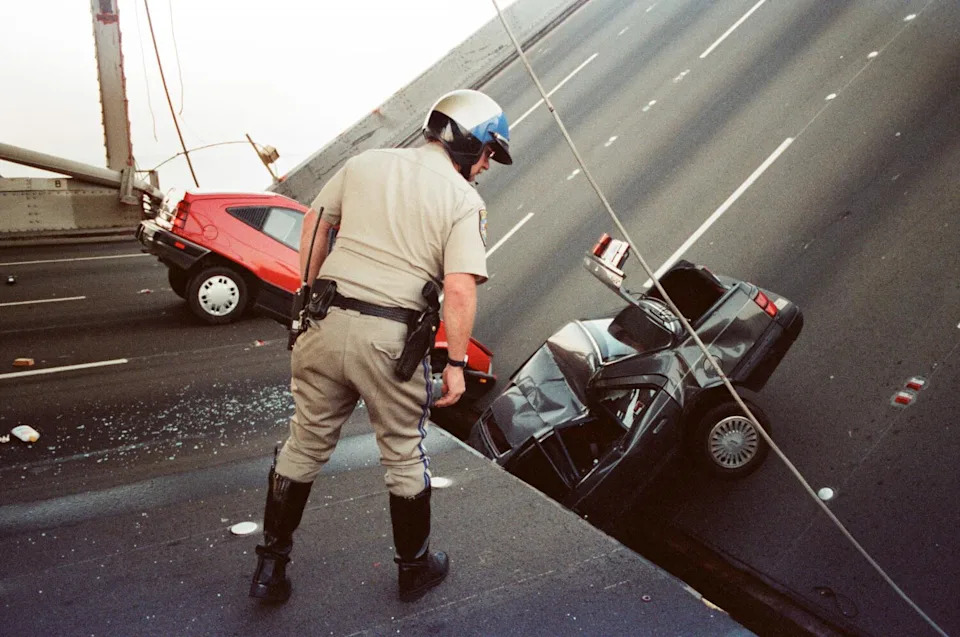 A man looks at cars damage by the partial collapse of the Bay Bridge after an earthquake.