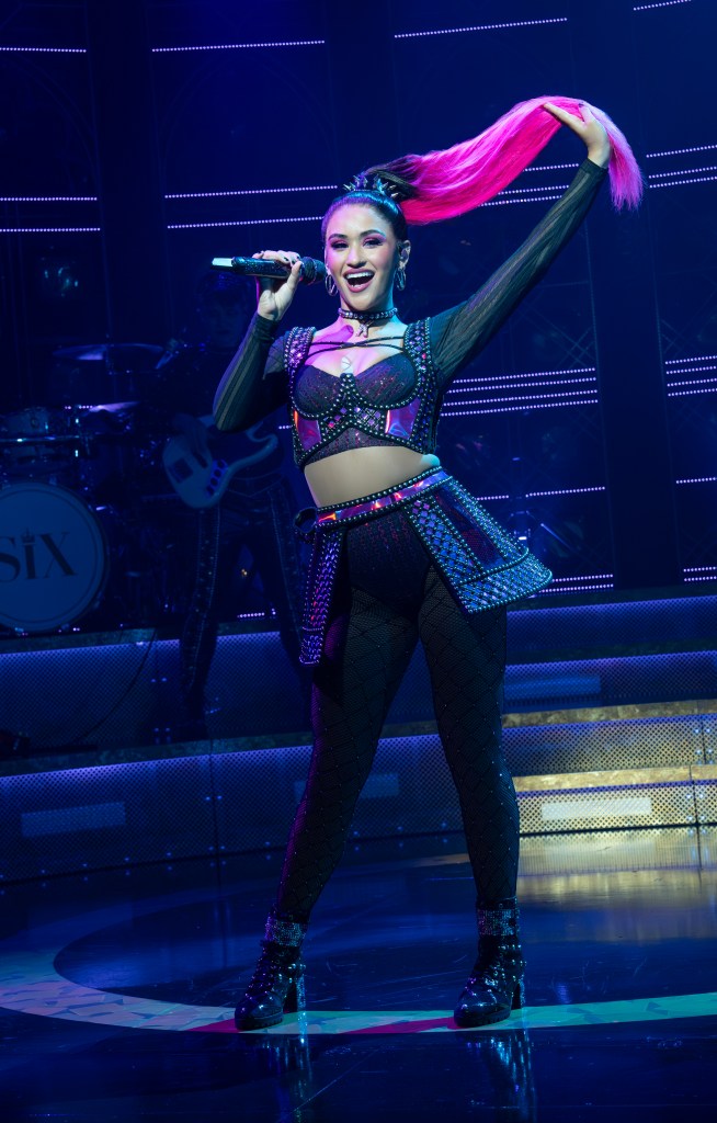 A woman grabs her long hot pink ponytail while singing into a mic