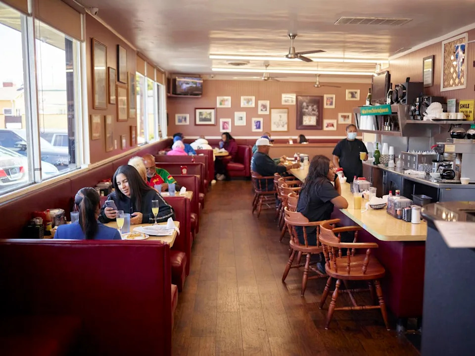 Two owners of a restaurant chat with a guest at the bar seating.